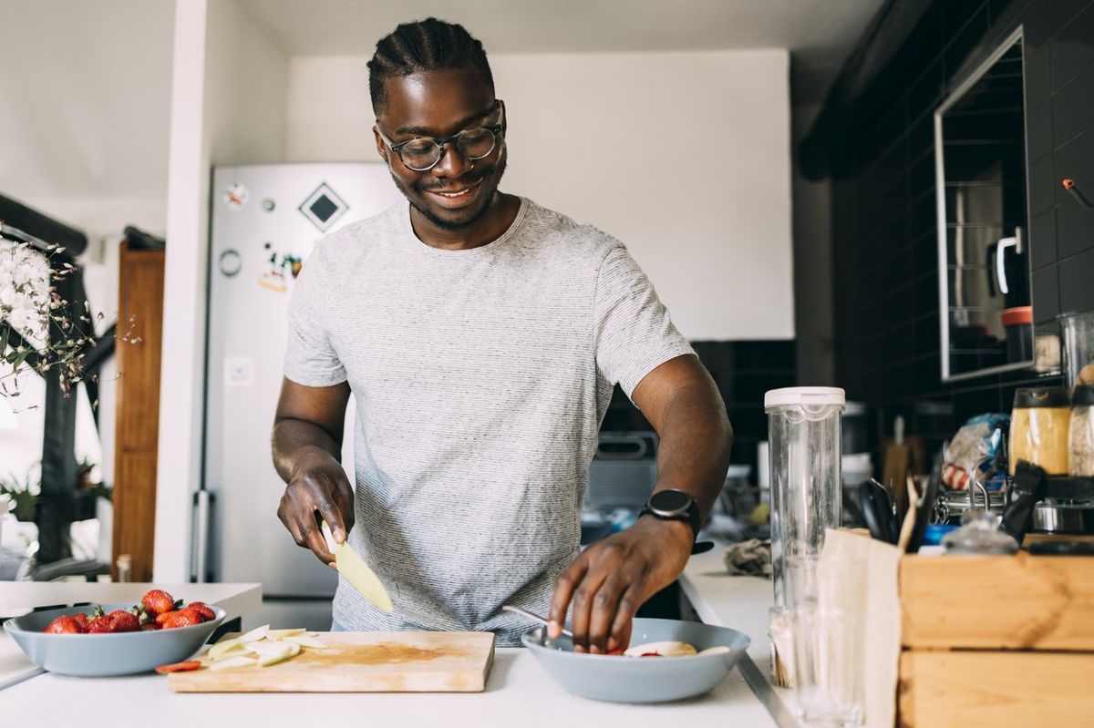 smiling African-American male cutting fruit while making a healthy meal.