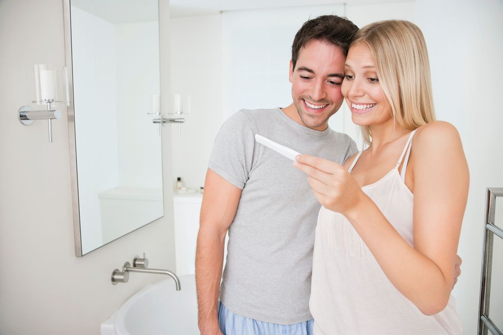 Smiling couple in bathroom, looking at pregnancy test