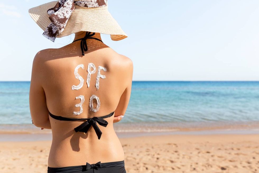 Spf 30 word is drawn with sunblock on woman's back relaxing at the beach