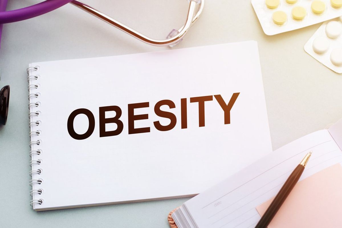 Stethoscope, pills and notebook with OBESITY word on medical desk.