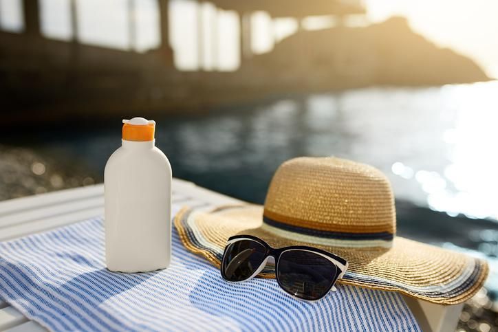 Botol krim matahari dan kacamata hitam di handuk pantai dengan pantai 