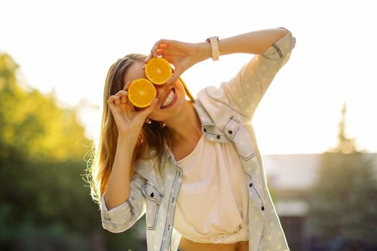 teen holding oranges in front of her eyes