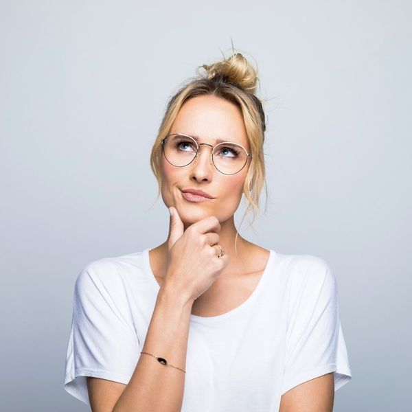 Thoughtful blond woman with hand on chin looking up against gray background