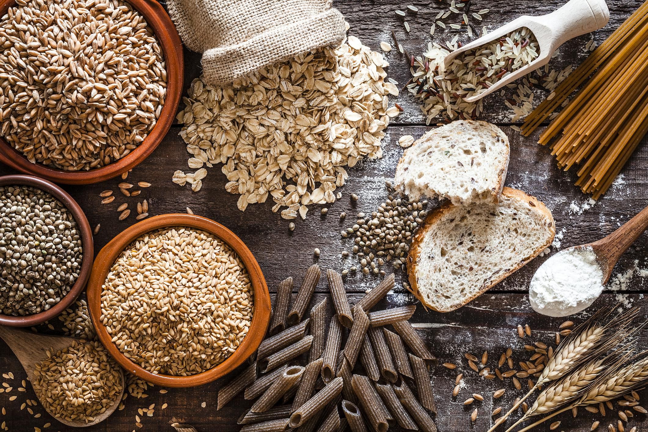 Top view of wholegrain and cereal composition shot on rustic wooden table. This type of food is rich of fiber and is ideal for dieting. The composition includes wholegrain sliced bread, various kinds of wholegrain pasta, wholegrain crackers, grissini, oat flakes, brown rice, spelt and flax seeds. Predominant color is brown.