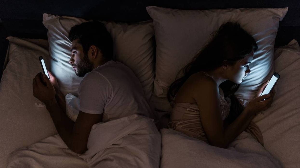 Top view of young couple lying in bed at night and using smartphones