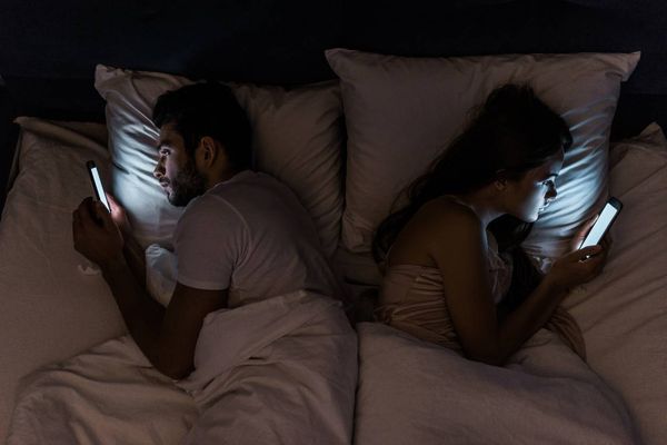 Top view of young couple lying in bed at night and using smartphones