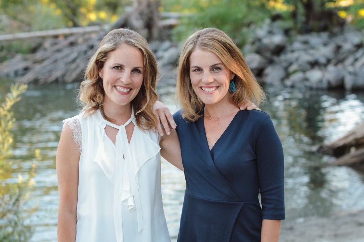 Twin sisters Joy Thomas and Jenelle Landgraf are standing next to each other in front of a body of water and nature.