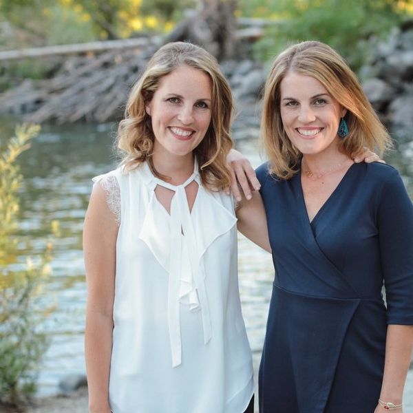 Twin sisters Joy Thomas and Jenelle Landgraf are standing next to each other in front of a body of water and nature.