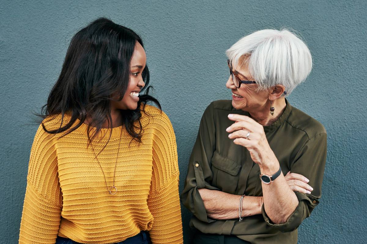 two cheerful businesswomen having a discussion while standing against a wall outdoors
