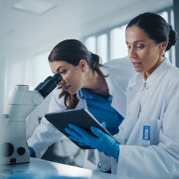 Two Female Scientists Working Together Using Microscope, Analyzing Samples, Talking