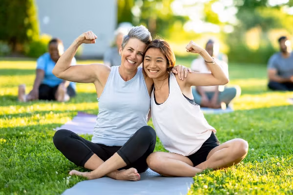 Two friends embrace and smile at an outdoor yoga class