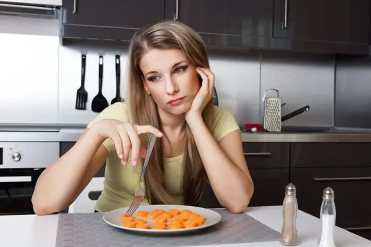 unhappy woman sitting in front of a plate of carrots