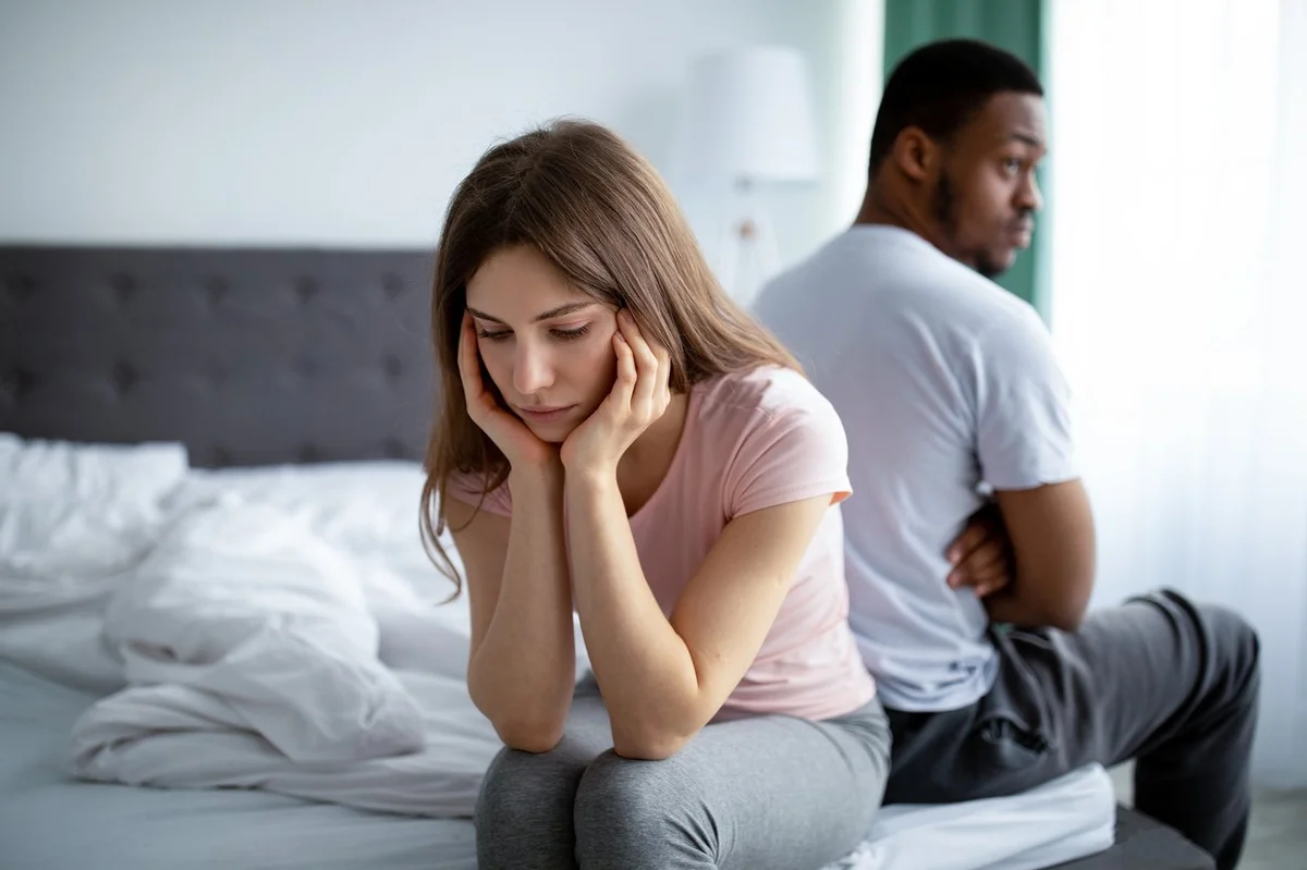 Upset Caucasian woman sitting back to back on bed with her black husband