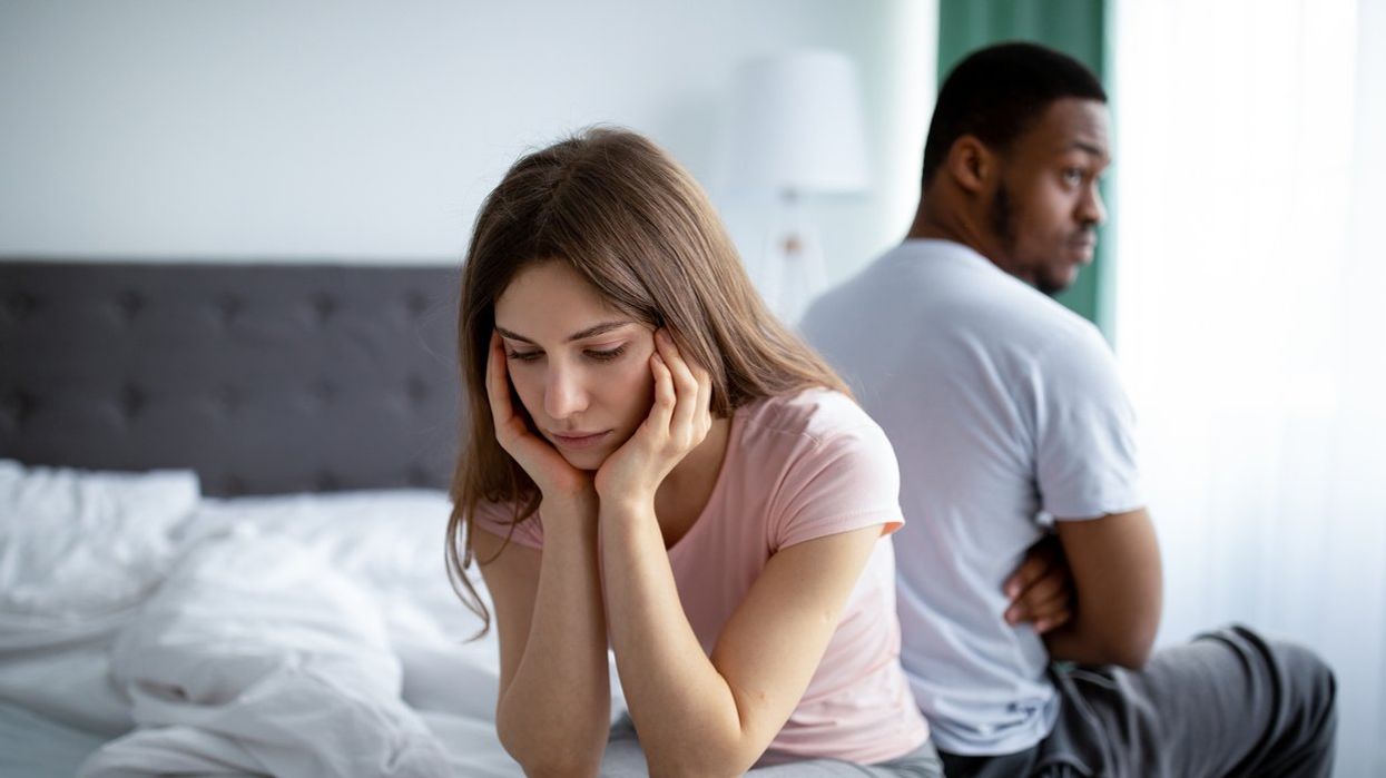 Upset Caucasian woman sitting back to back on bed with her black husband