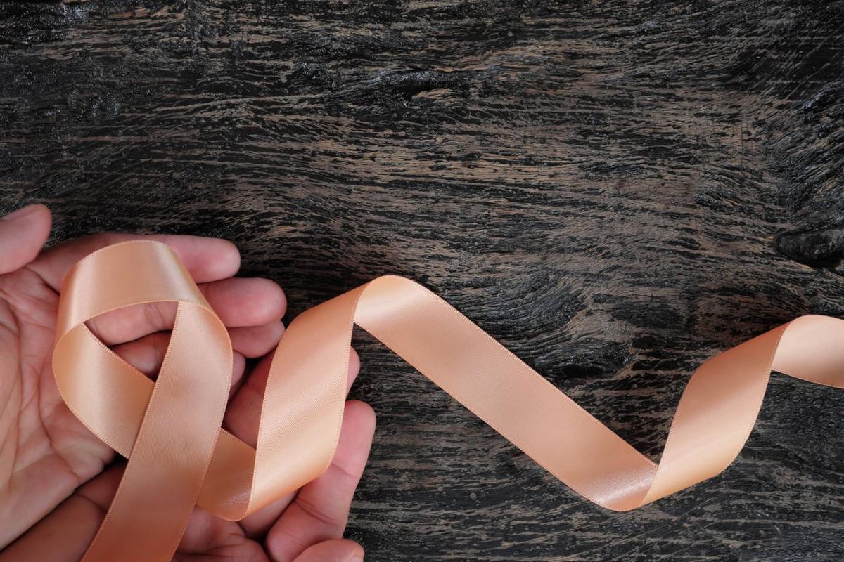 view of hand holding peach ribbon on dark wood background