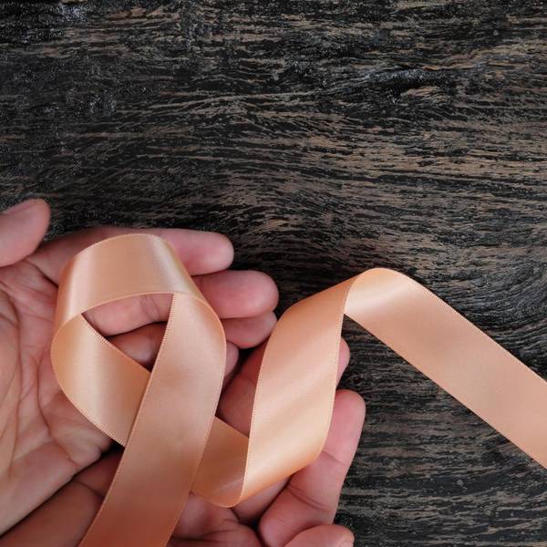 view of hand holding peach ribbon on dark wood background
