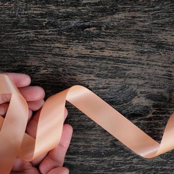 view of hand holding peach ribbon on dark wood background