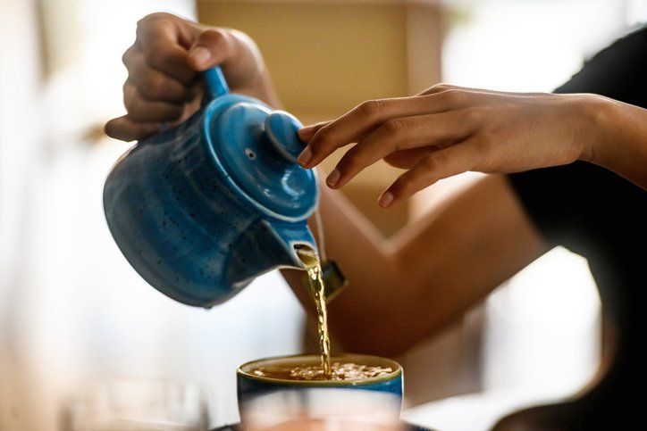 waitress carefully pours hot tea from the tea pot into the ceramic cup