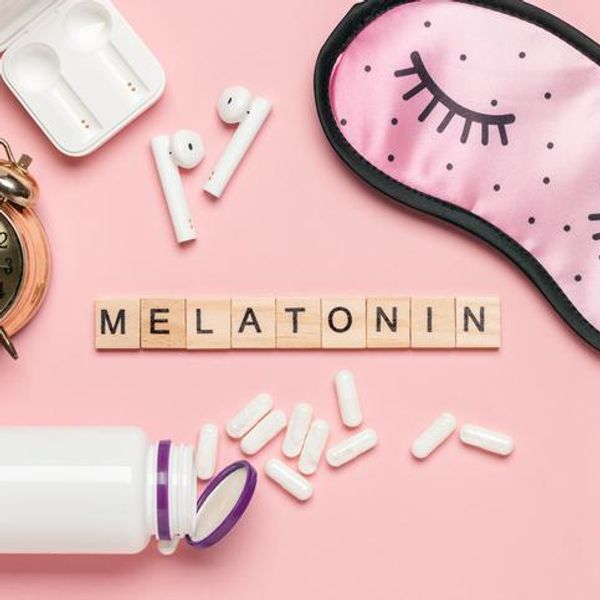 White bottle and pills, letters Melatonin, alarm clock and sleep mask on light grey background