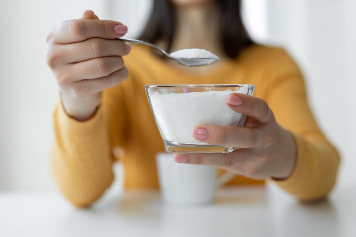 Woman adding refined sugar to cup of coffee