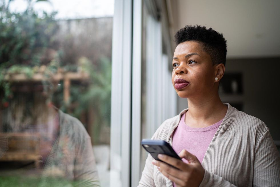 Woman contemplating using smartphone at home