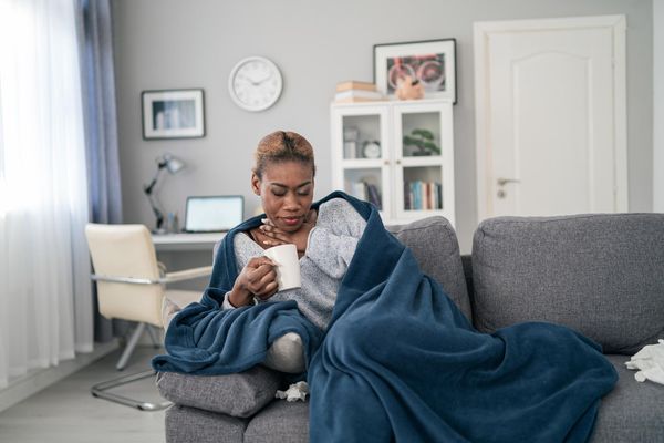 woman, covered with blanket, having a fever and sore throat, holding a cup with hot drink
