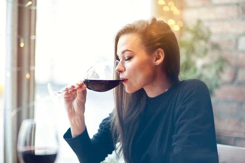woman drinking red wine with friends in cafe, portrait with wine glass near window