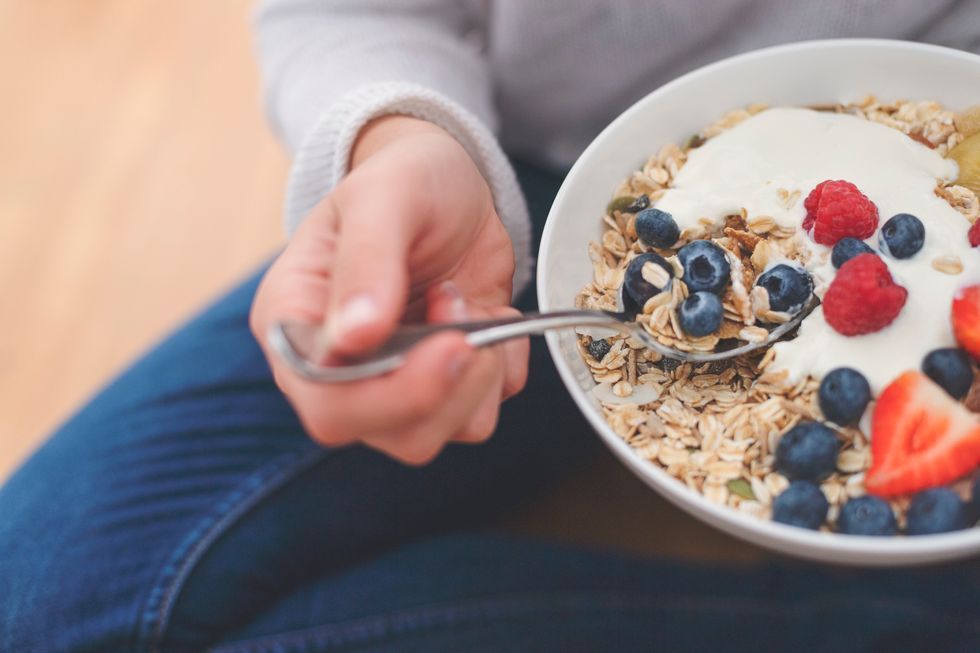 Woman Eating healthy breakfast bowl. It includes strawberries, blueberries, kiwifruit, granola, muesli and yoghurt