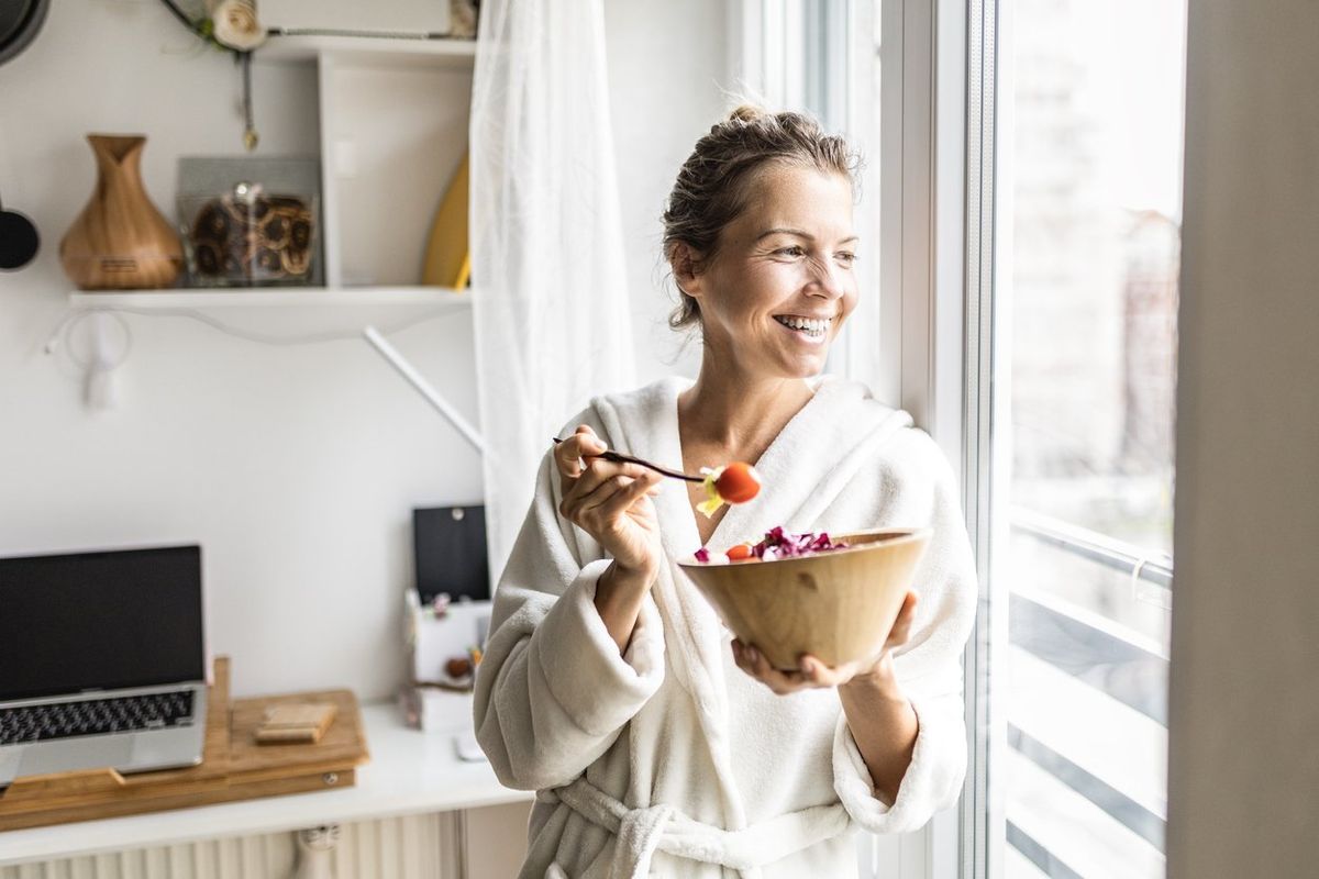 woman eating healthy vegetable salad wearing bathrobe