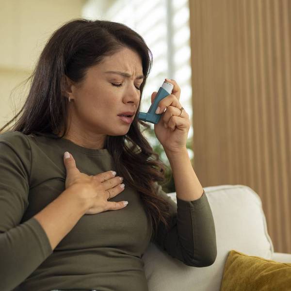 Woman experiencing asthma attack using inhaler at home