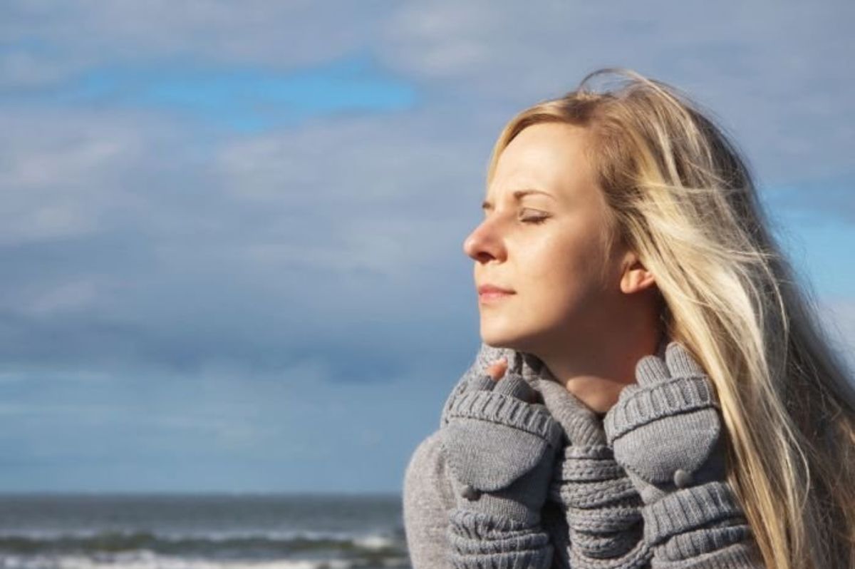 woman facing the sun wearing winter clothes at the beach