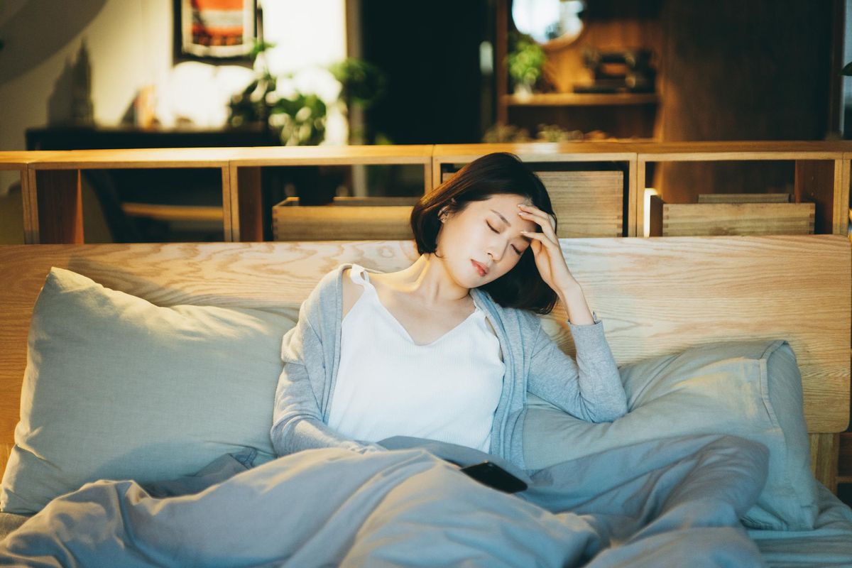 woman feeling sick and suffering from a headache, lying on the bed