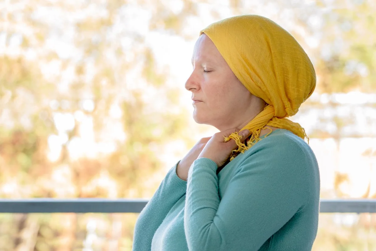 woman from behind putting a yellow scarf on her head because she has Urothelial Bladder cancer and worried