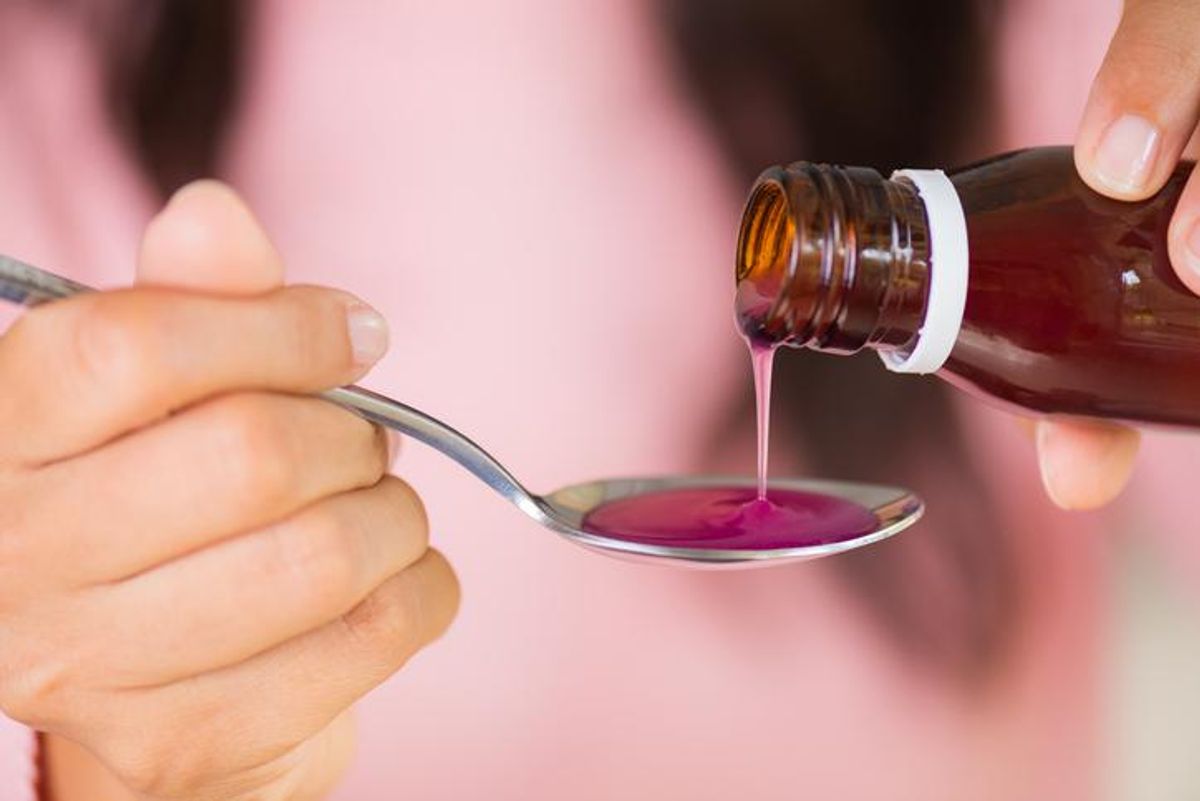 Woman hand pouring medication or antipyretic syrup from bottle to spoon