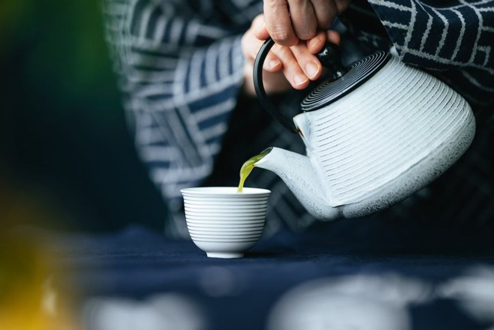 Tangan seorang wanita menuangkan teh hijau matcha dari teko ke dalam cangkir