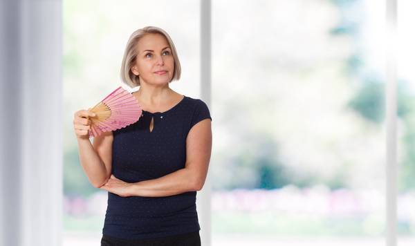 woman holding a fan having a hot flash