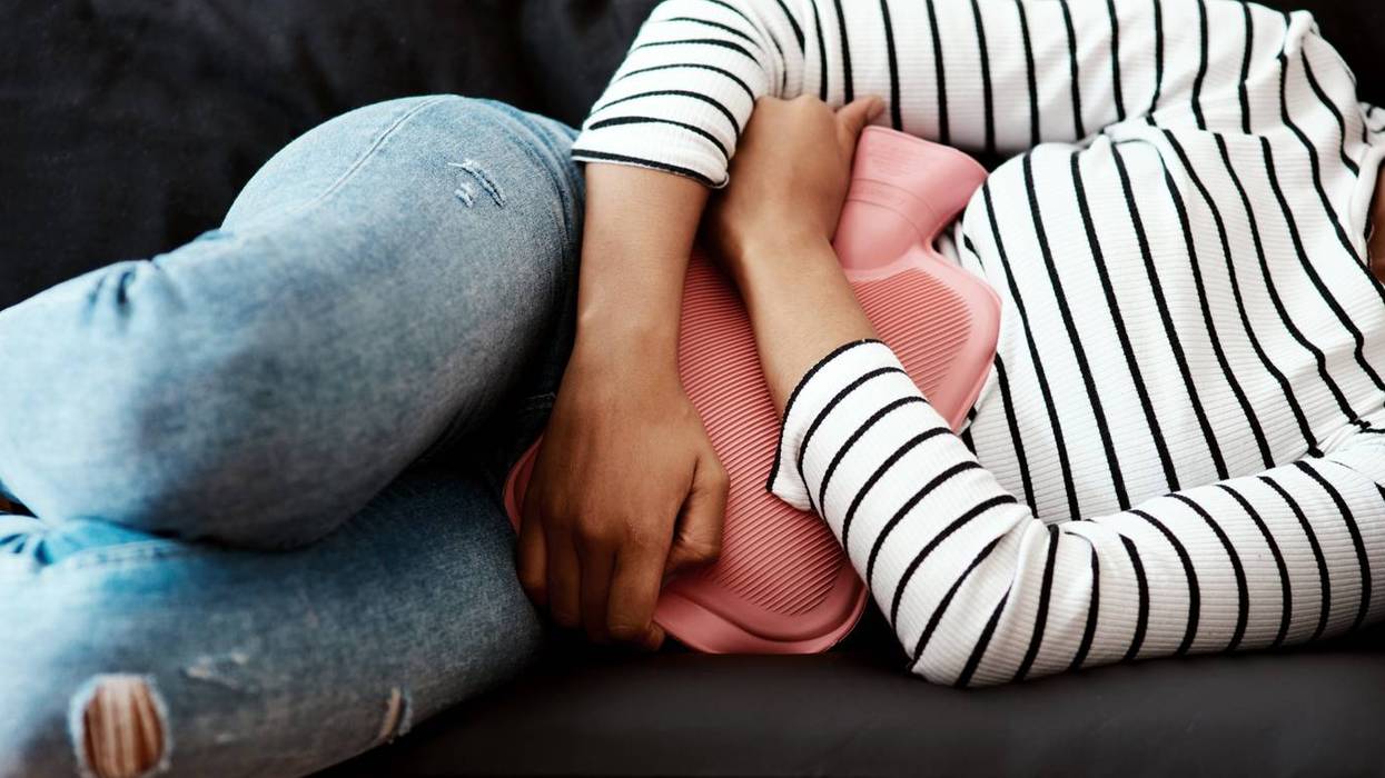 woman holding a hot water bottle against her stomach on the sofa at home