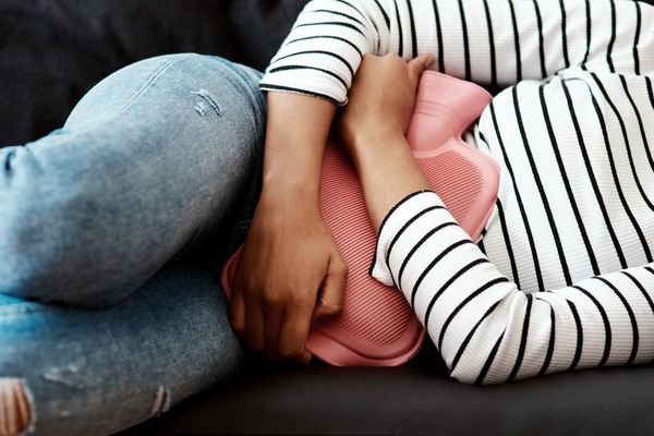 woman holding a hot water bottle against her stomach on the sofa at home