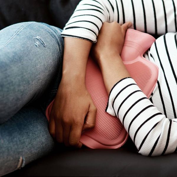 woman holding a hot water bottle against her stomach on the sofa at home