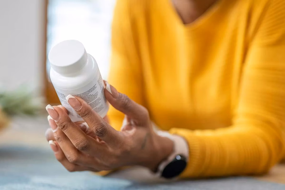 Woman holding medications in hands and checking instruction on vitamin bottle