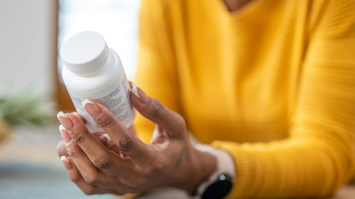 Woman holding medications in hands and checking instruction on vitamin bottle