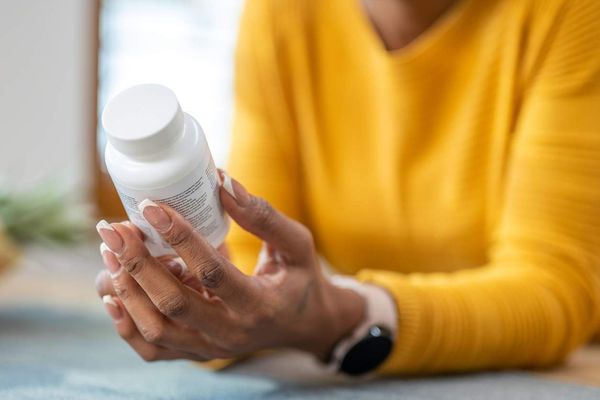Woman holding medications in hands and checking instruction on vitamin bottle