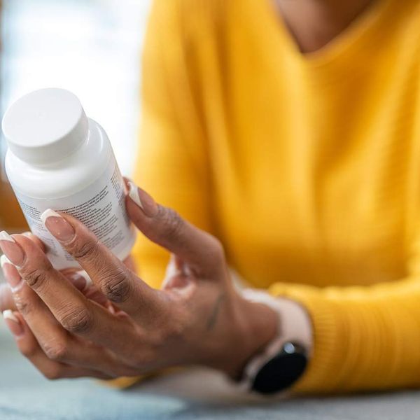 Woman holding medications in hands and checking instruction on vitamin bottle
