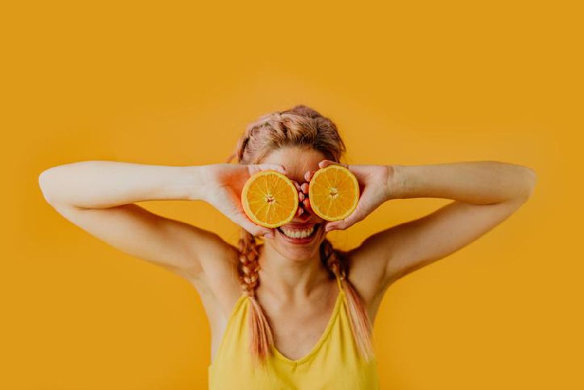 woman holding orange halves in front of her eyes