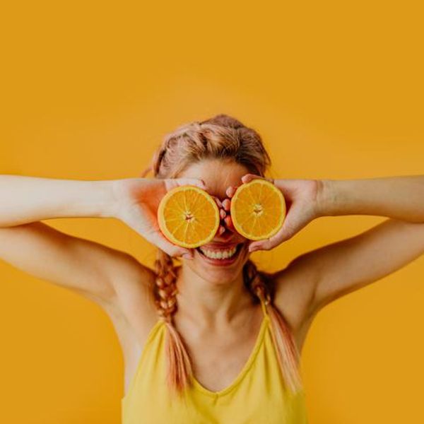 woman holding orange halves in front of her eyes