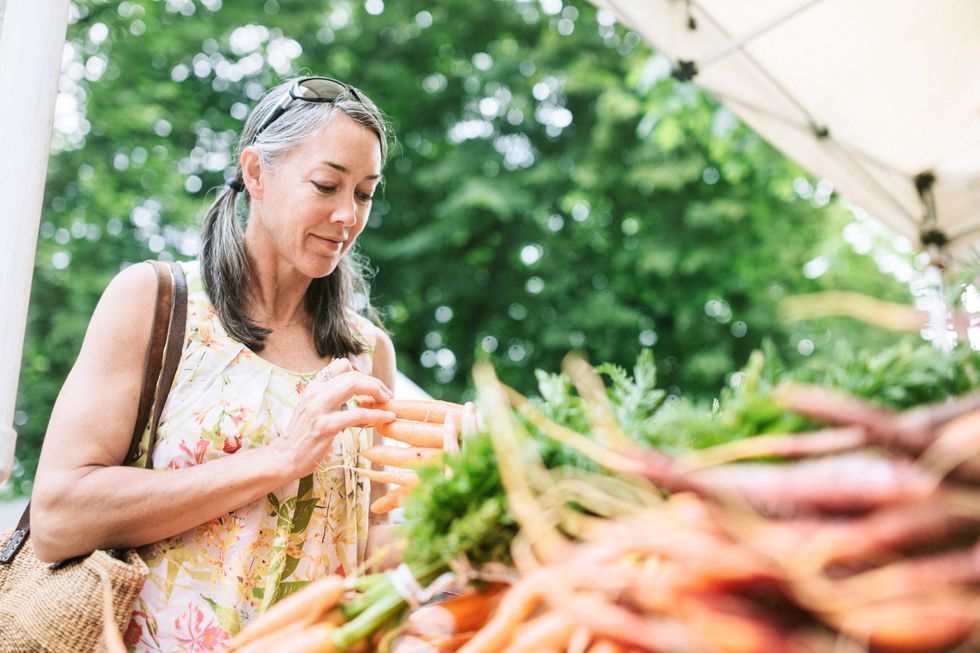 woman in her 50's shops in a local outdoor agriculture market with fresh, organic local fruits and vegetables
