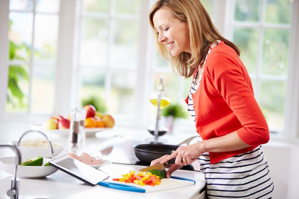 Woman In Kitchen Following Recipe On Digital Tablet To Make A Meal