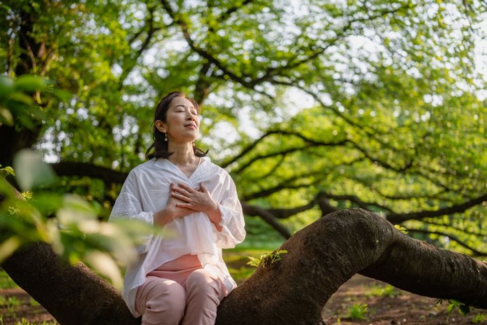 Seorang wanita menutup matanya, berlatih latihan pernapasan dan bermeditasi di alam.