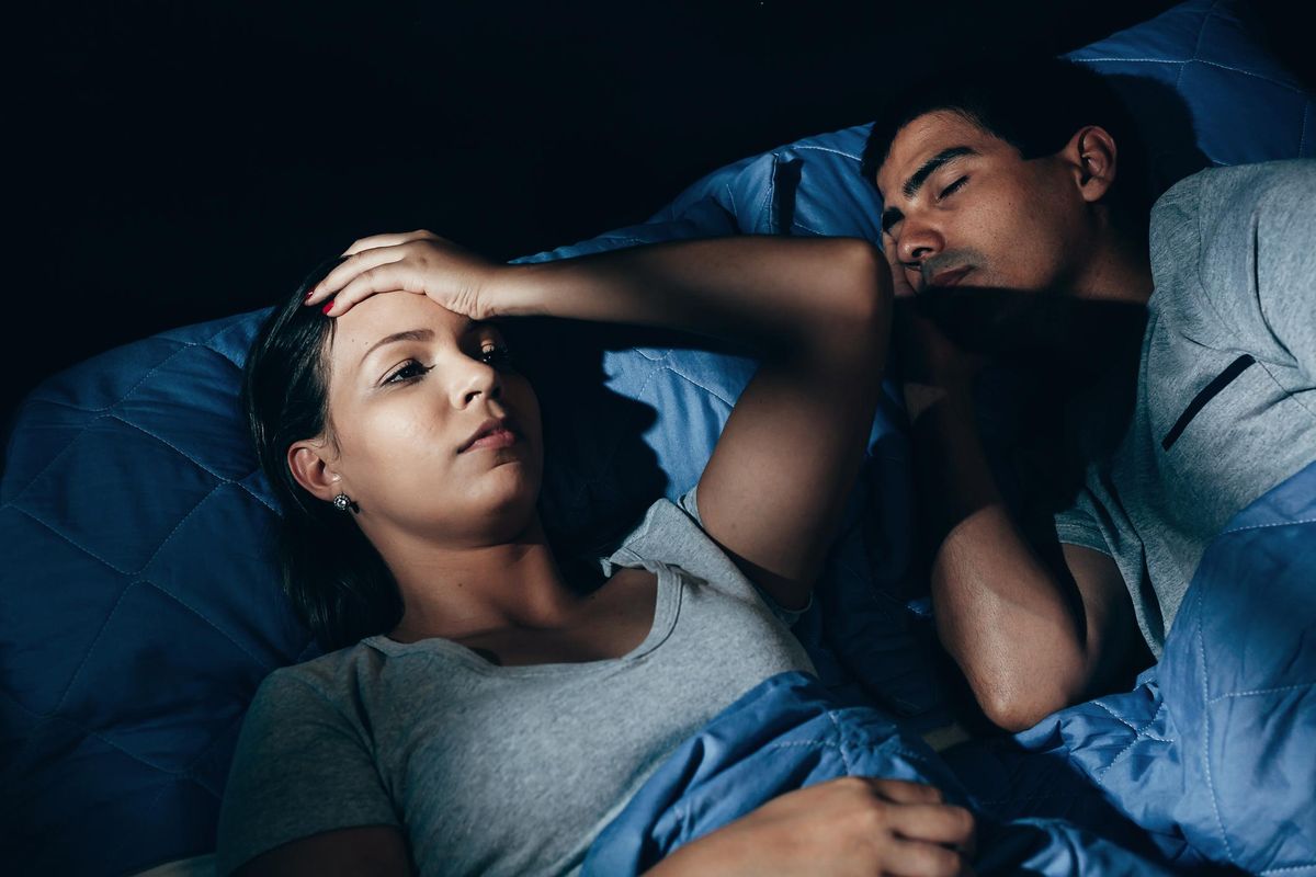 Woman laying awake distressed, sleeping next to her male partner. 