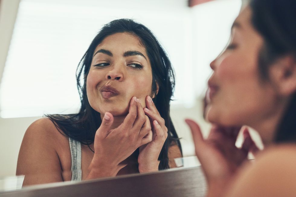 woman looking at her acne in the mirror